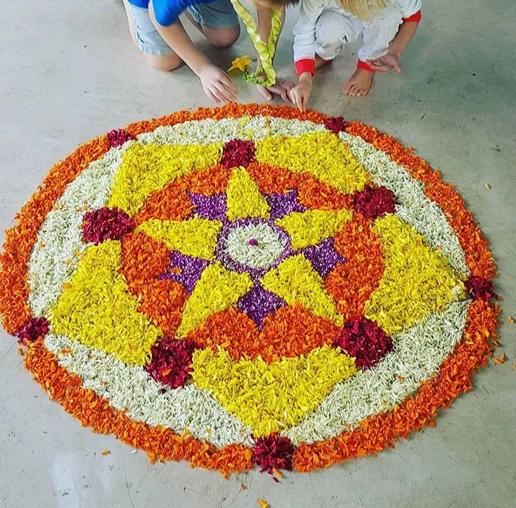 Two people making a beautiful circular star design pookolam