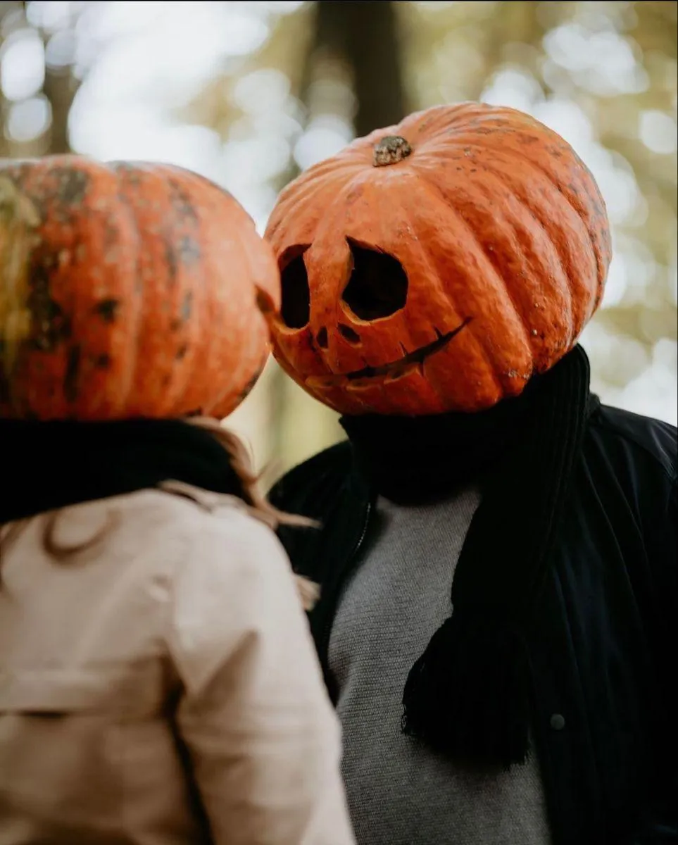 Two People Wearing Pumpkin Head Masks Interacting Outdoors
