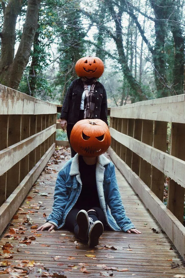 Two People with Carved Pumpkin Heads Posing on Wooden Bridge