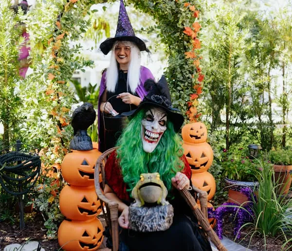 Two Women in Witch Costumes Posing with Pumpkins Outdoors