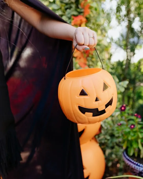 Woman Holding Pumpkin Bucket with Carved Faces Wallpaper