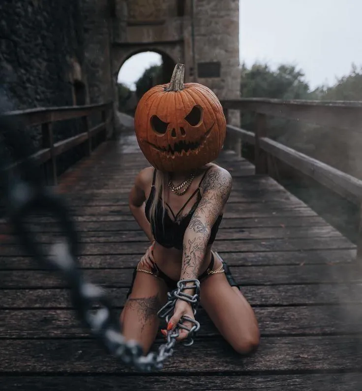 Woman with pumpkin head posing on wooden bridge in fall