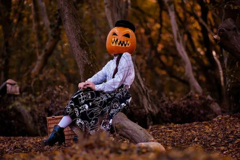 Woman with pumpkin head sitting near a tree in forest