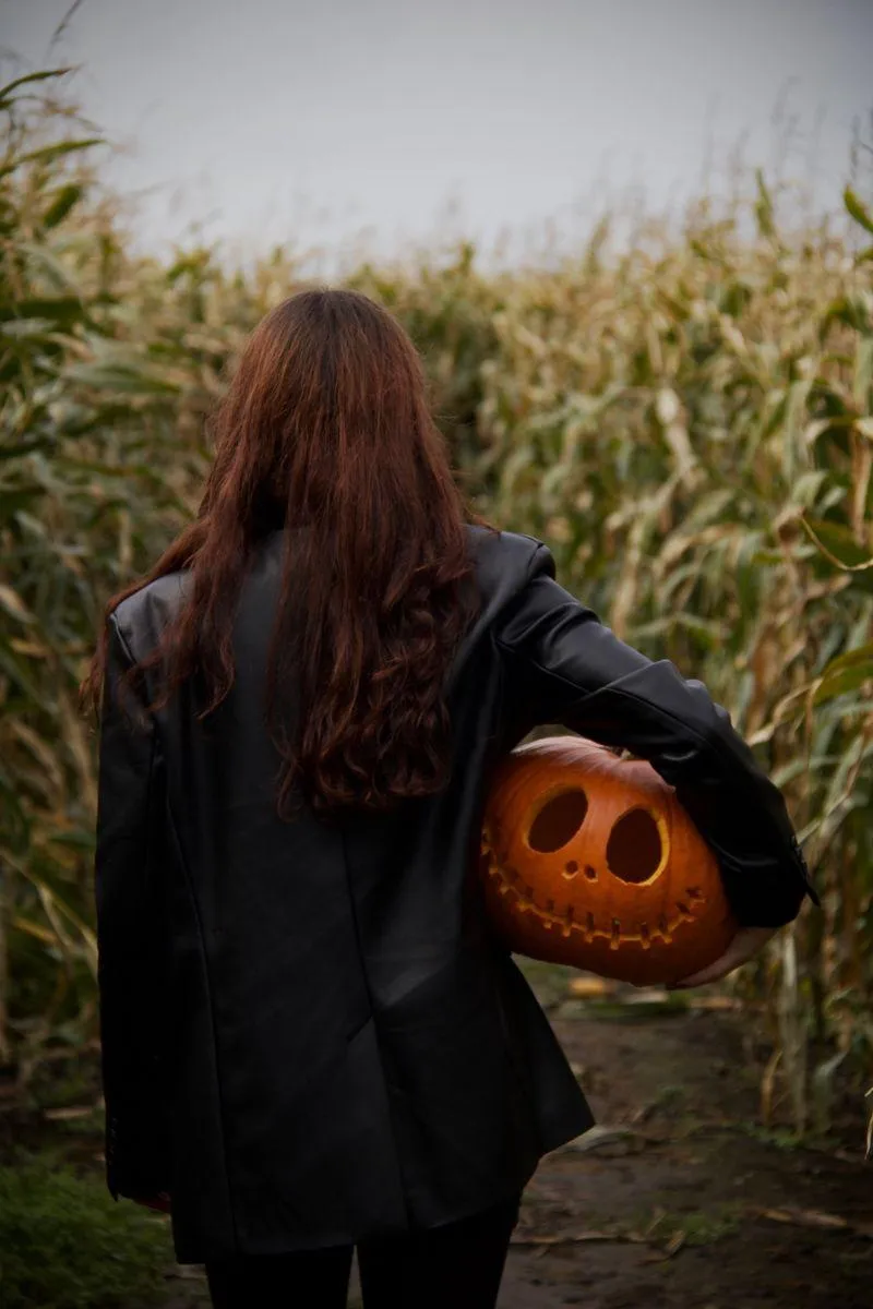Women holding a carved pumpkin walking through cornfield
