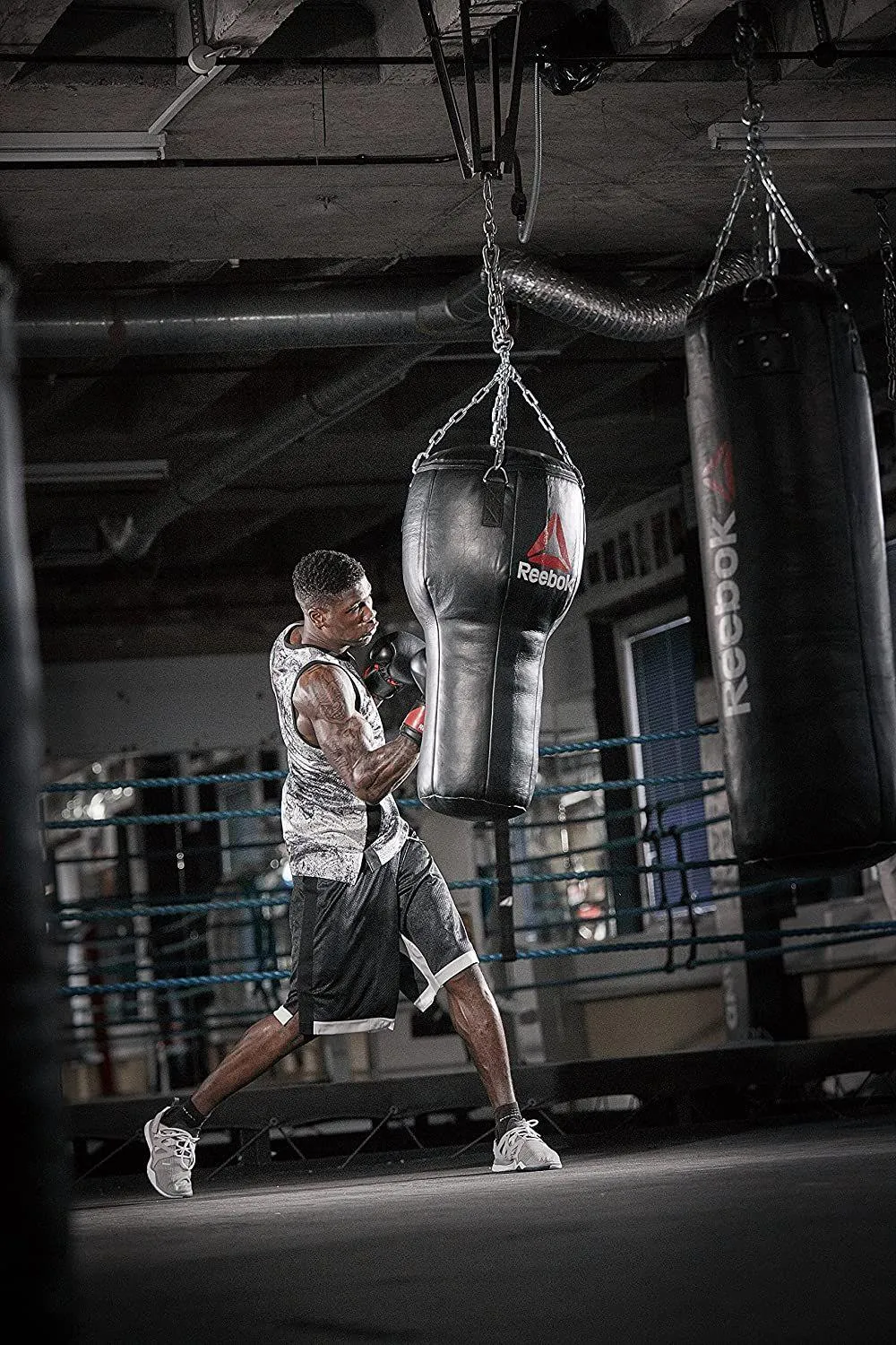 Boxer Training By Hitting a Punching Bag in a Dim Gym