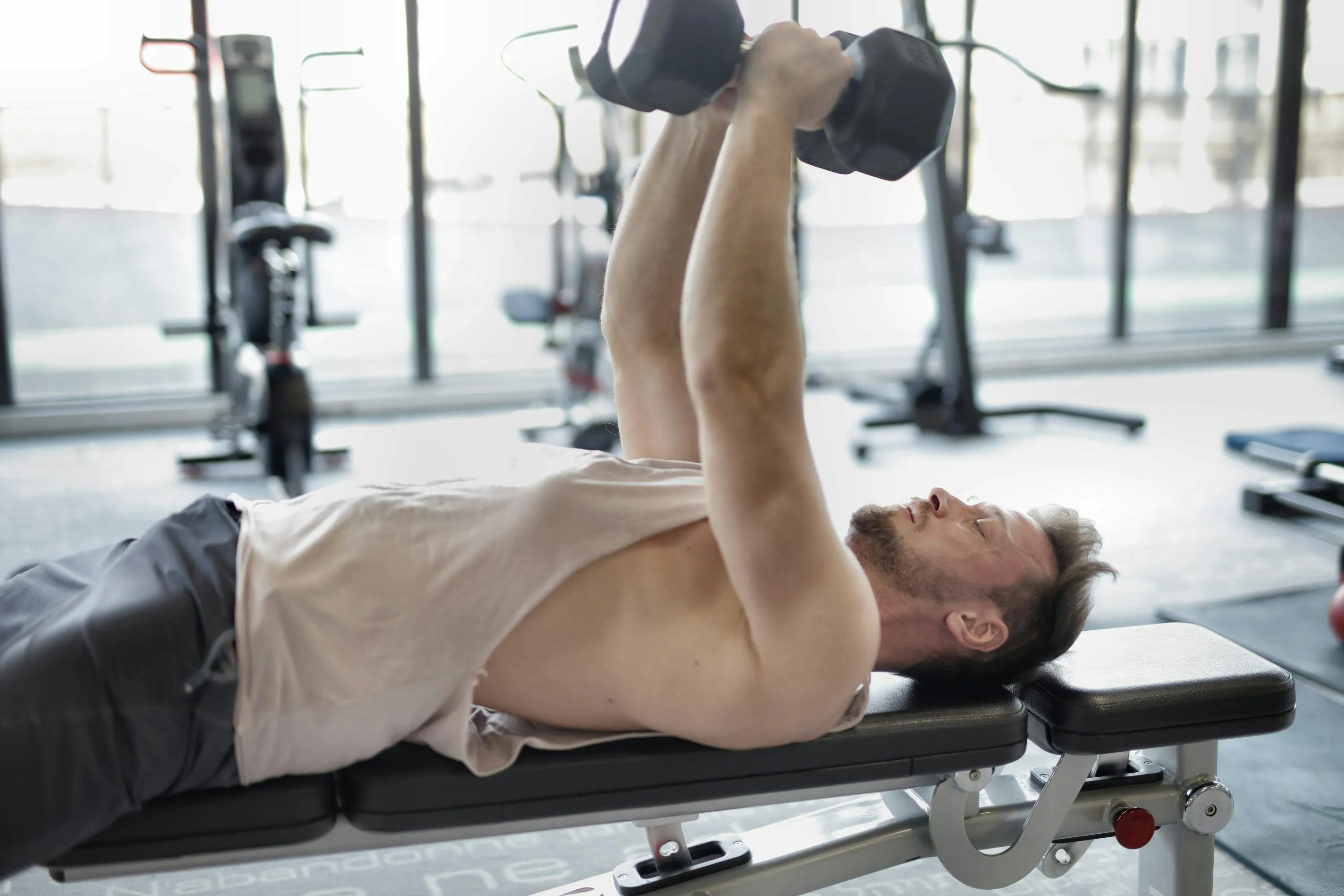 Man Lifting Dumbbells While Lying Flat on a Bench Gym
