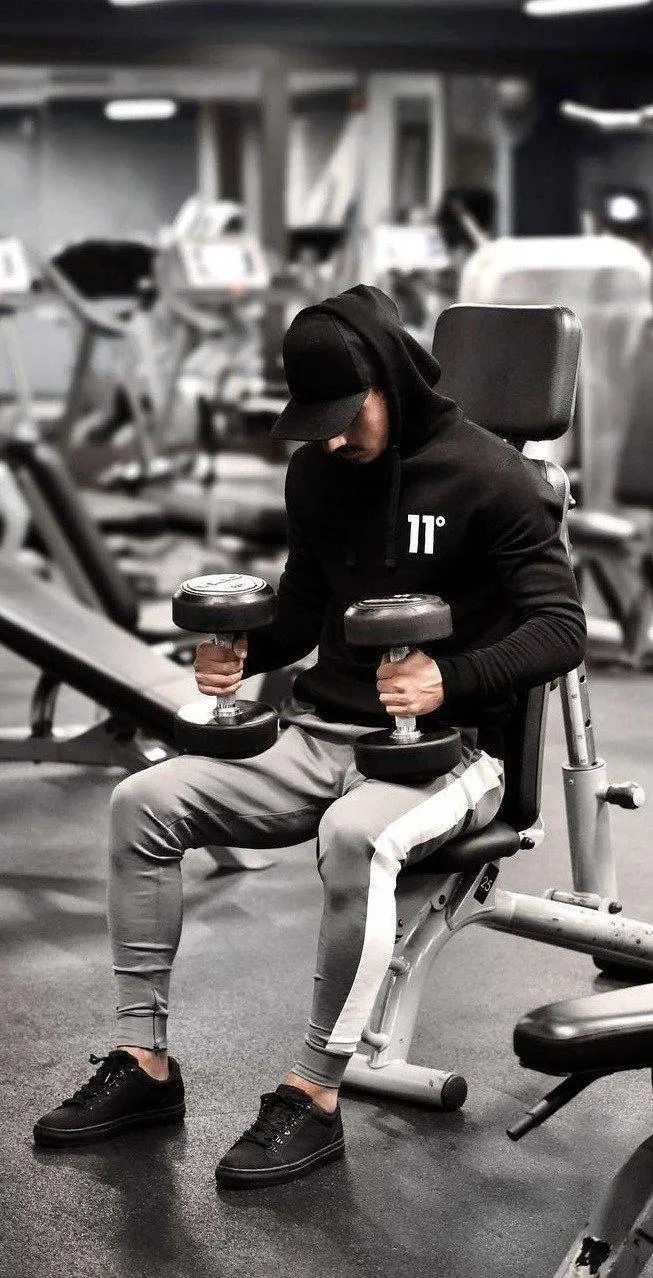 Man Seated in a Gym With a Hooded Jacket and Dumbbells