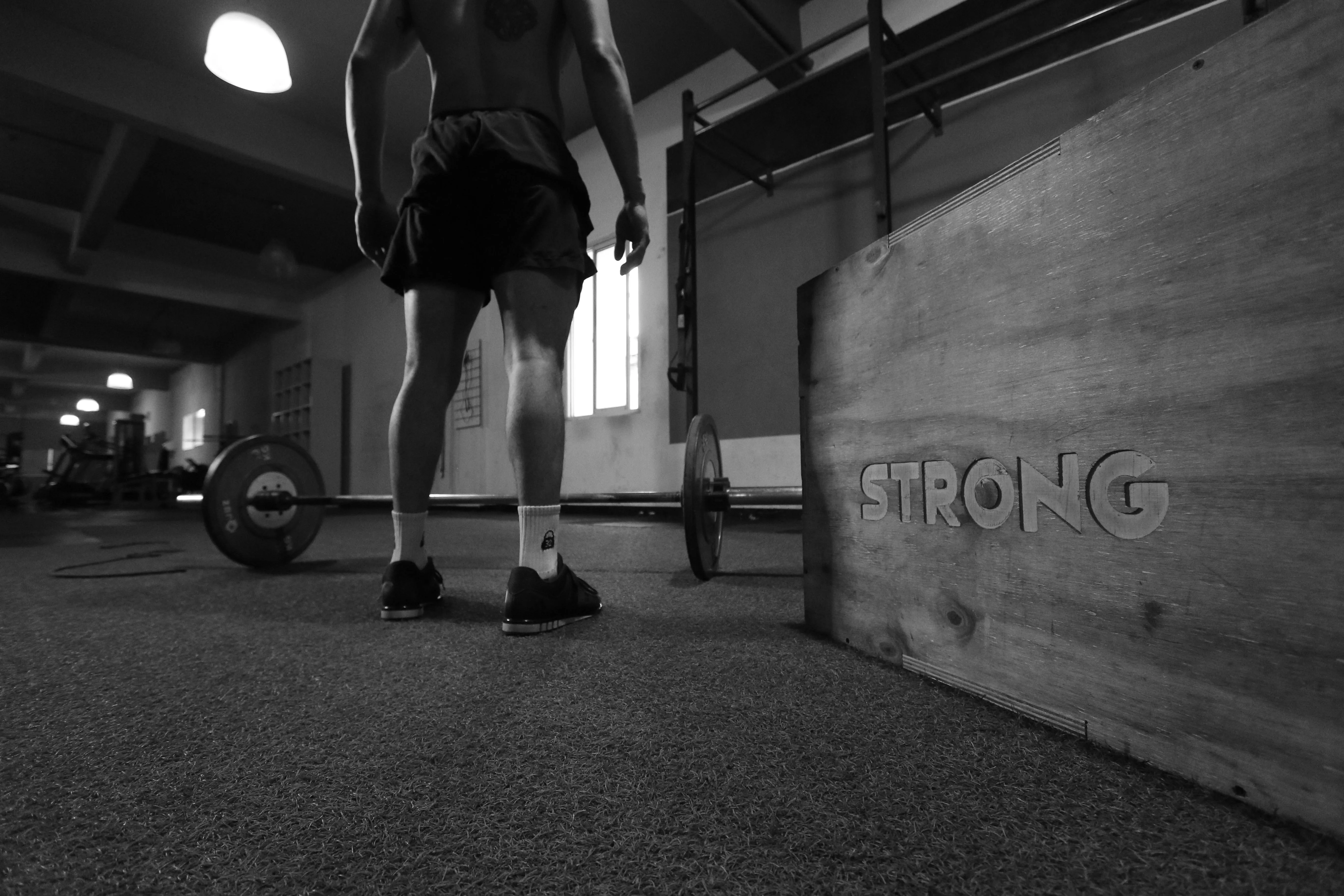 Man Stands Before Loaded Barbell Near Strong Sign in Gym