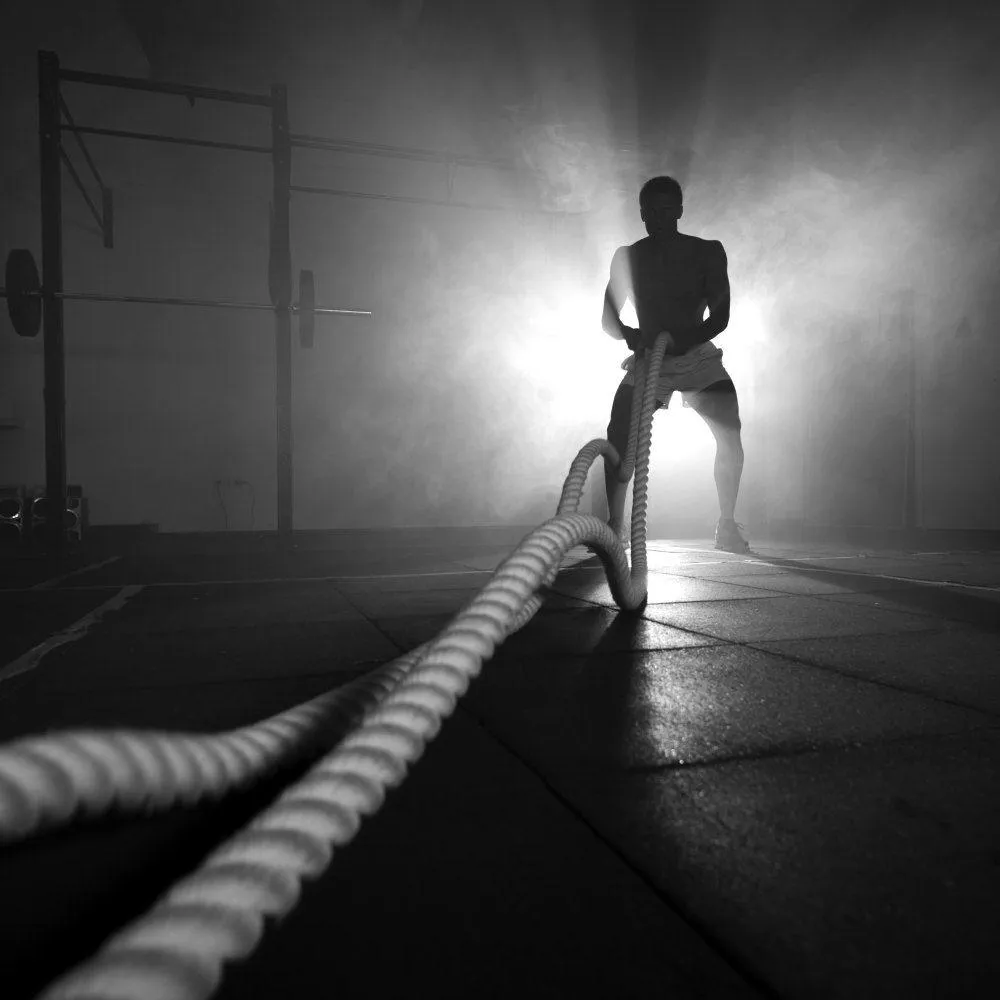 Man Using Battle Ropes in Dramatic Gym Lighting Wallpaper