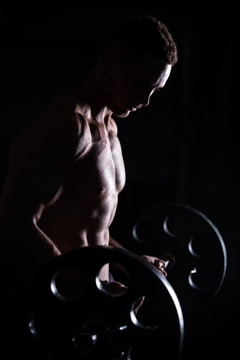 Muscular Man Lifting Weights in Dramatic Shadow Lighting