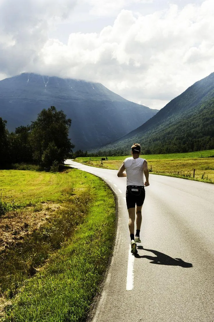 Person Jogging on the Road Surrounded By Green Hills