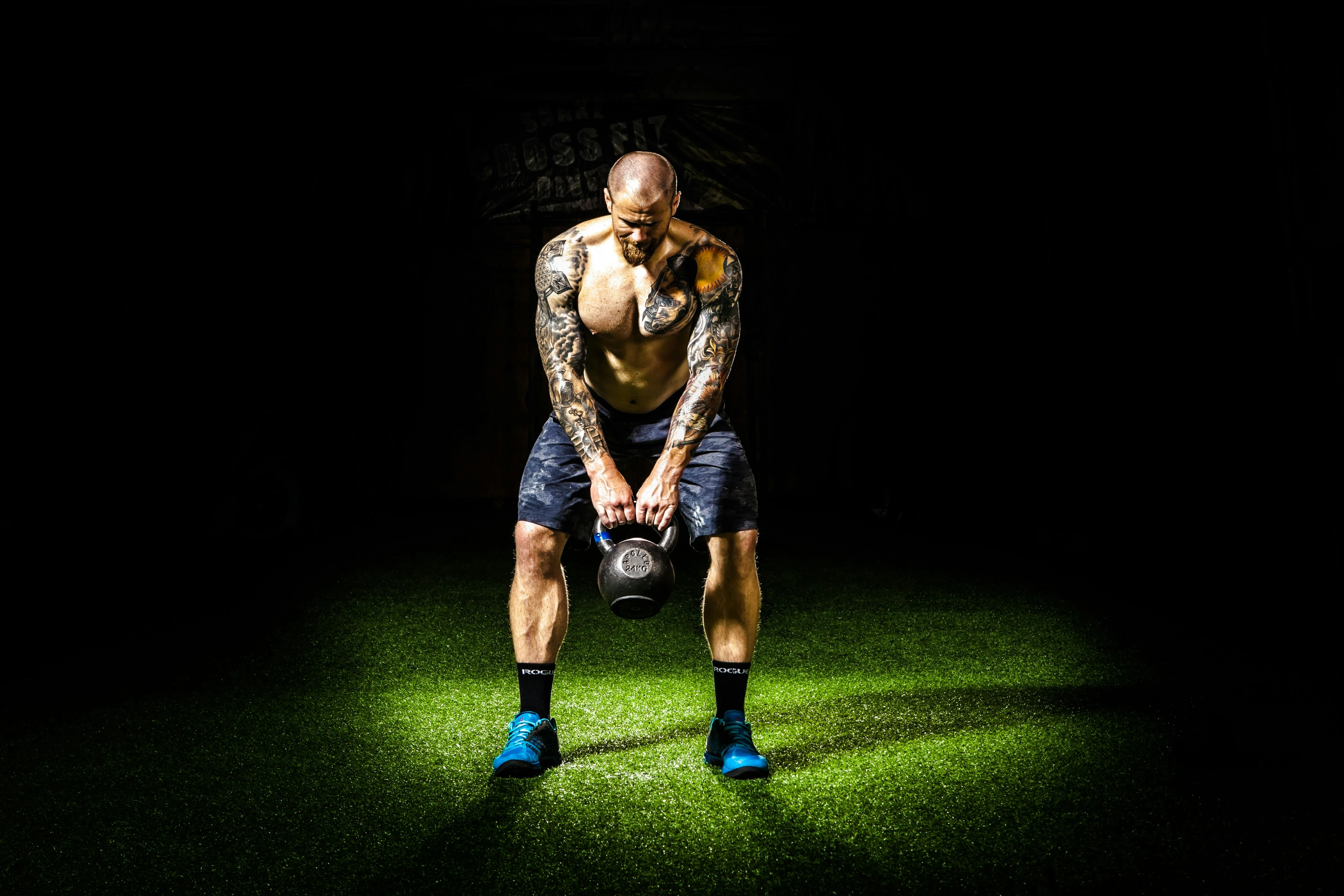 Tattooed Man Lifting a Kettlebell on Green Turf Spotlighted