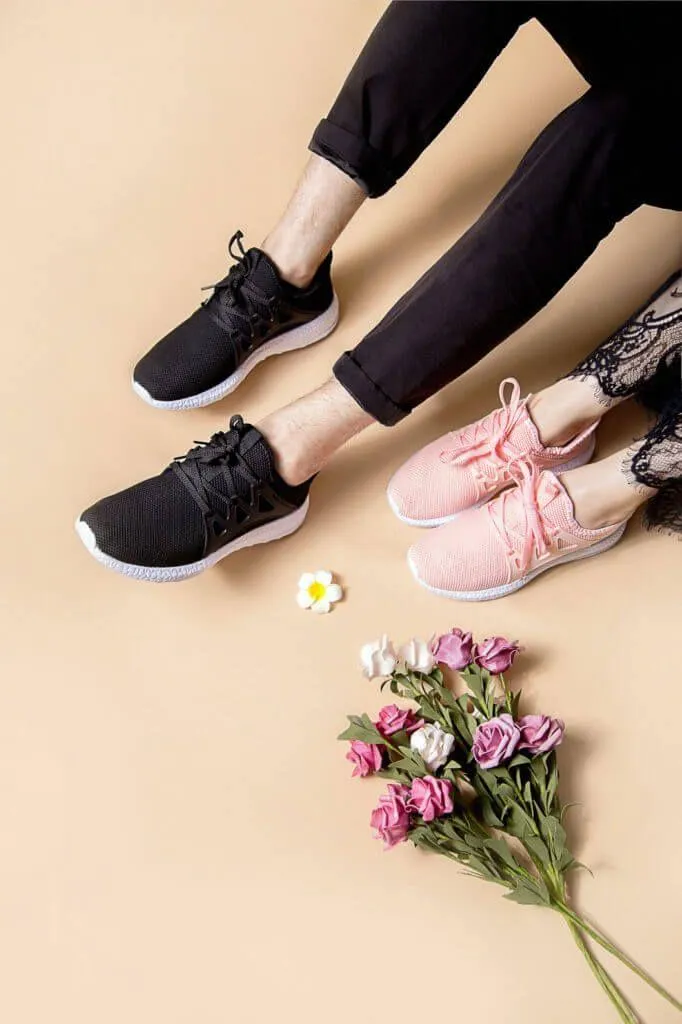 Two Pairs of Feet Wearing Sneakers Next To a Flower