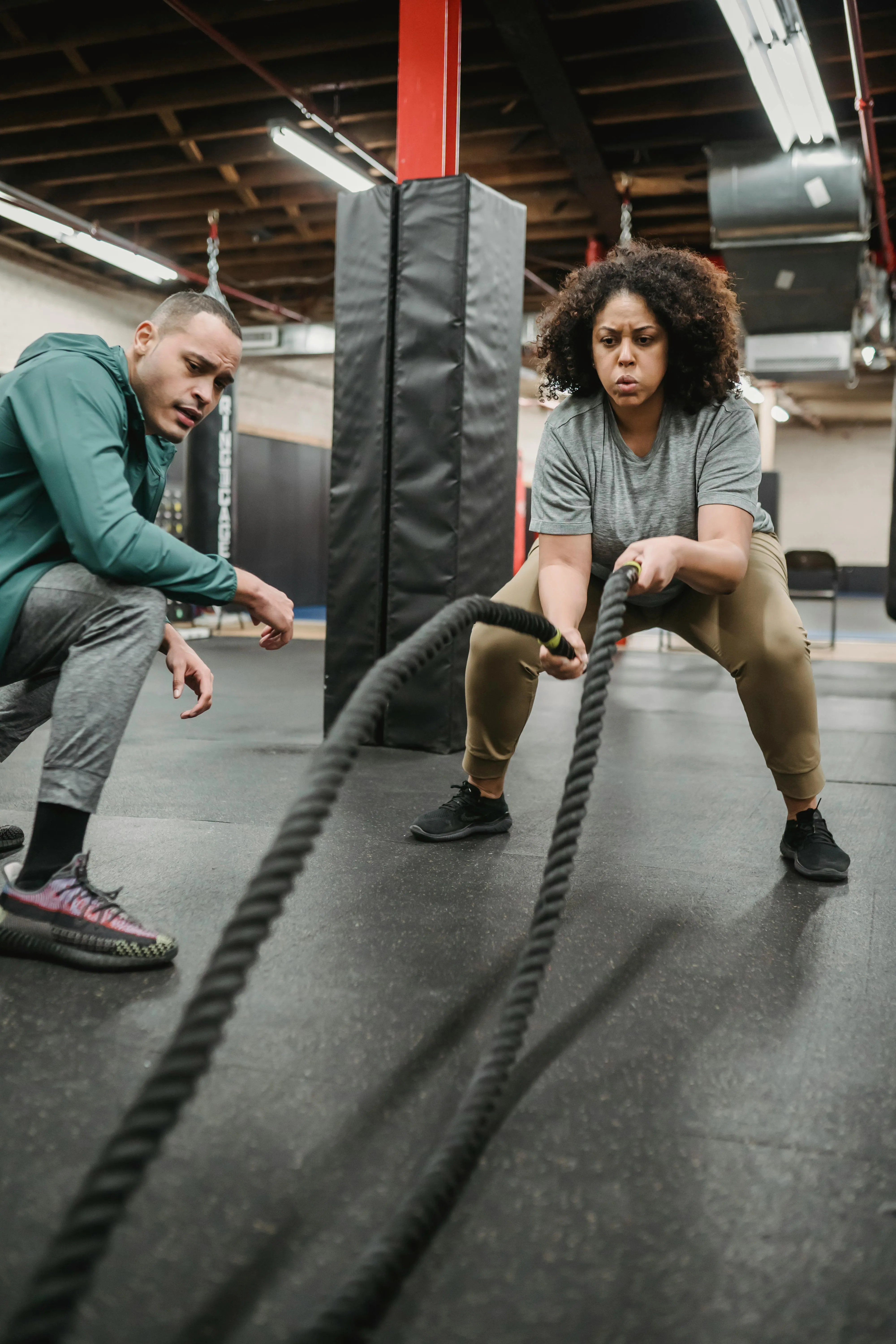 Woman Training Battle Ropes Under Guidance on the Gym Floor