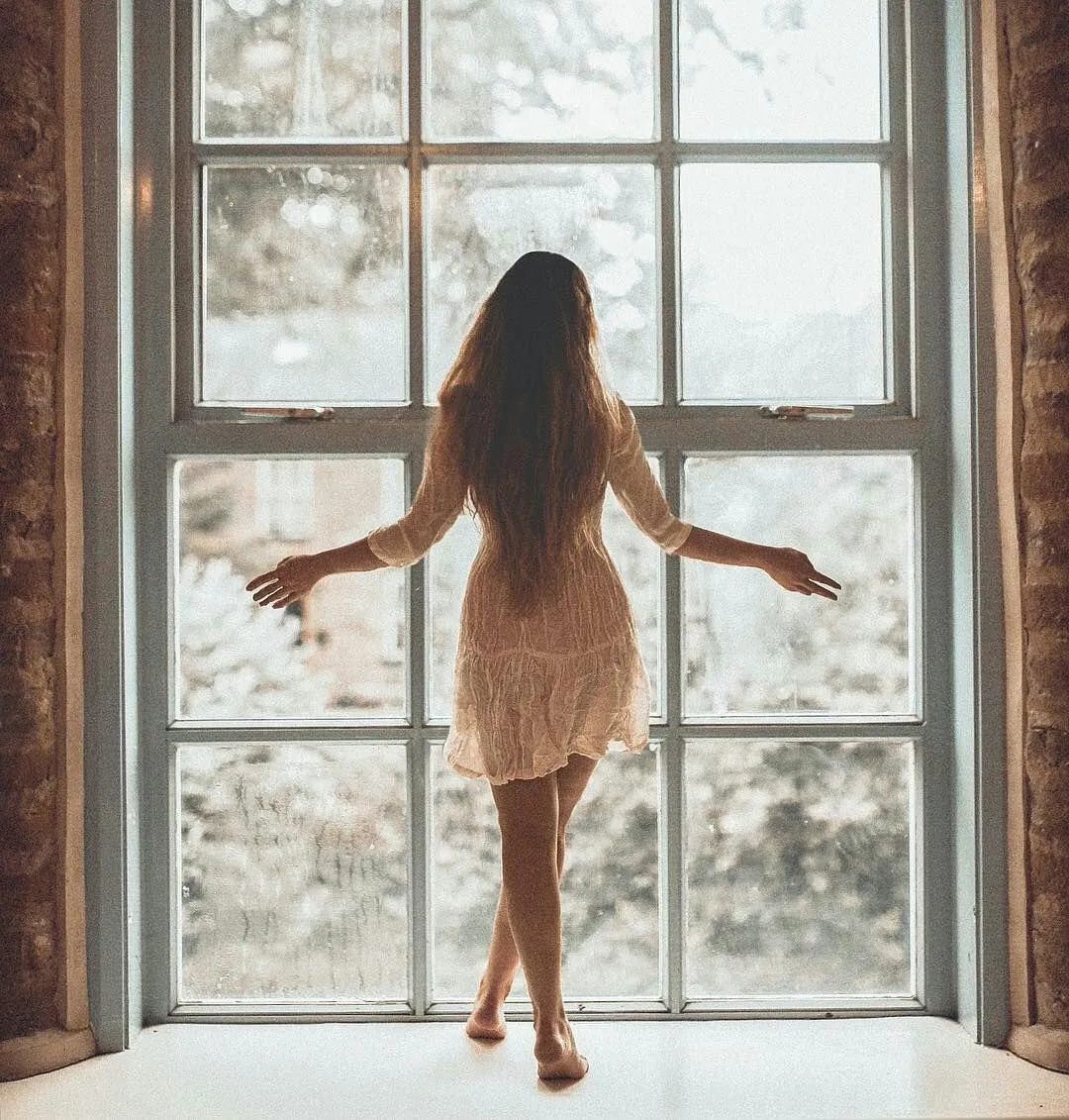 Backlit Silhouette of a Woman Standing by a Large Window