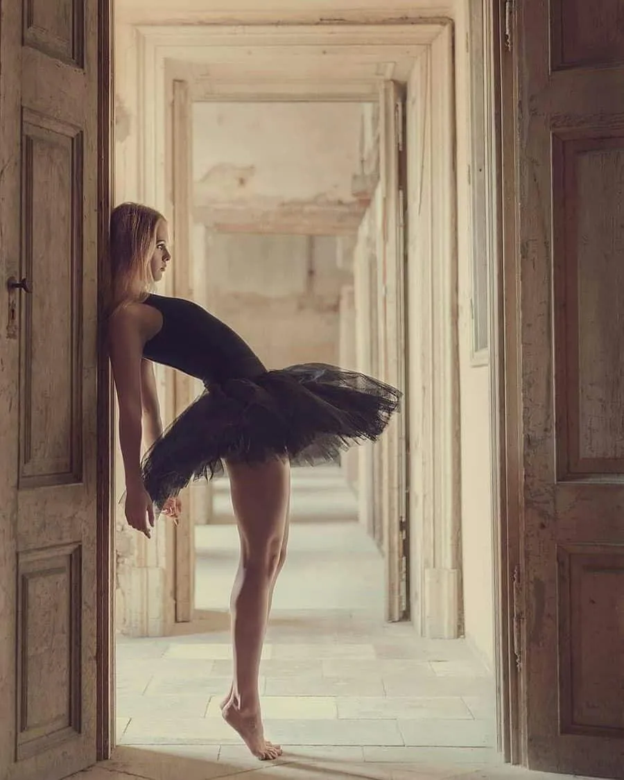 Ballet dancer in black tutu framed between rustic wood doors