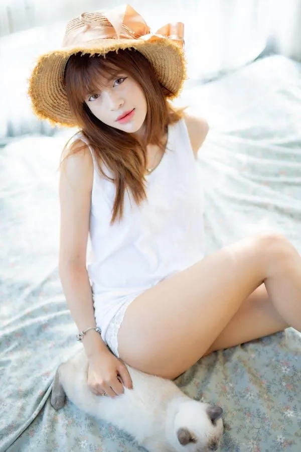 Beautiful woman sitting on the bed with a cat and a hat