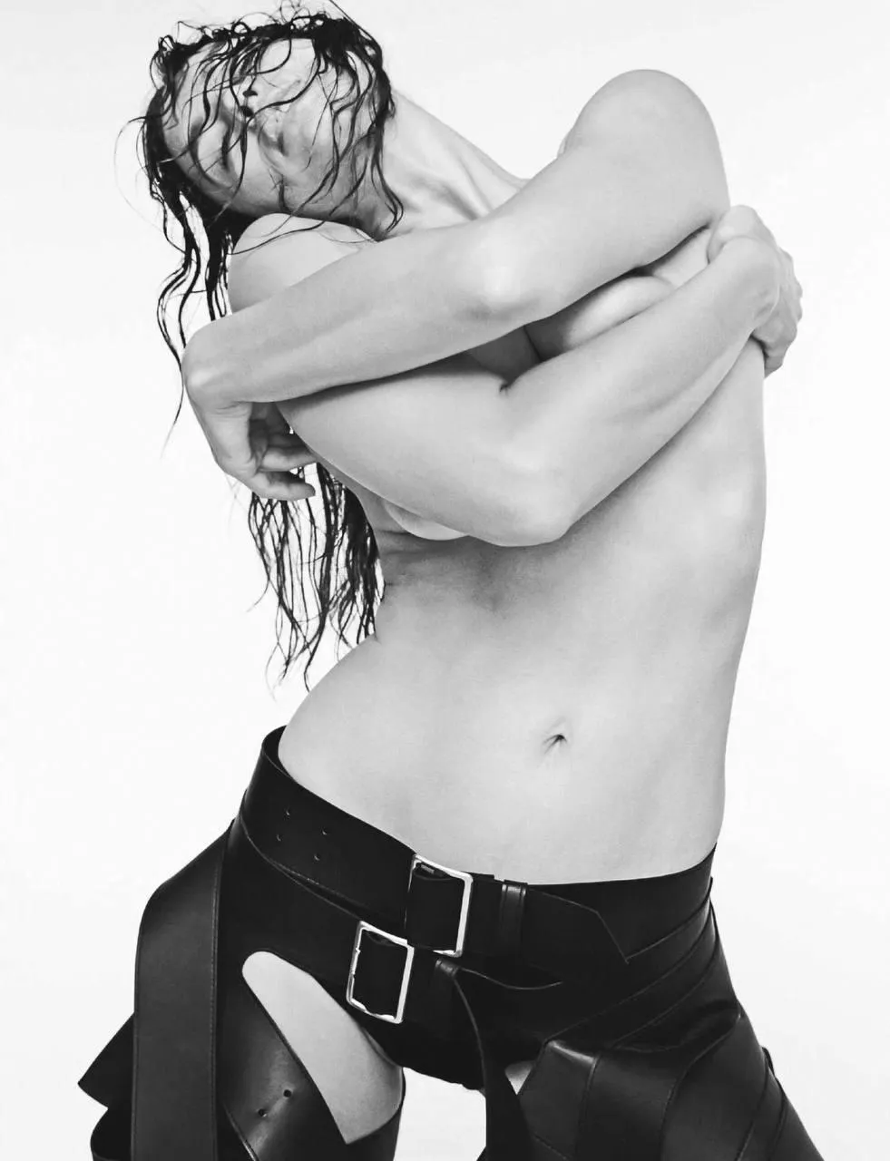 Black and white photo of a topless woman holding suspenders