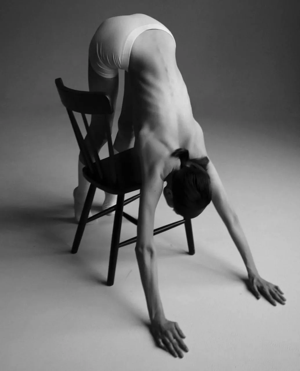 Black and white photo of a woman bending over a wooden chair