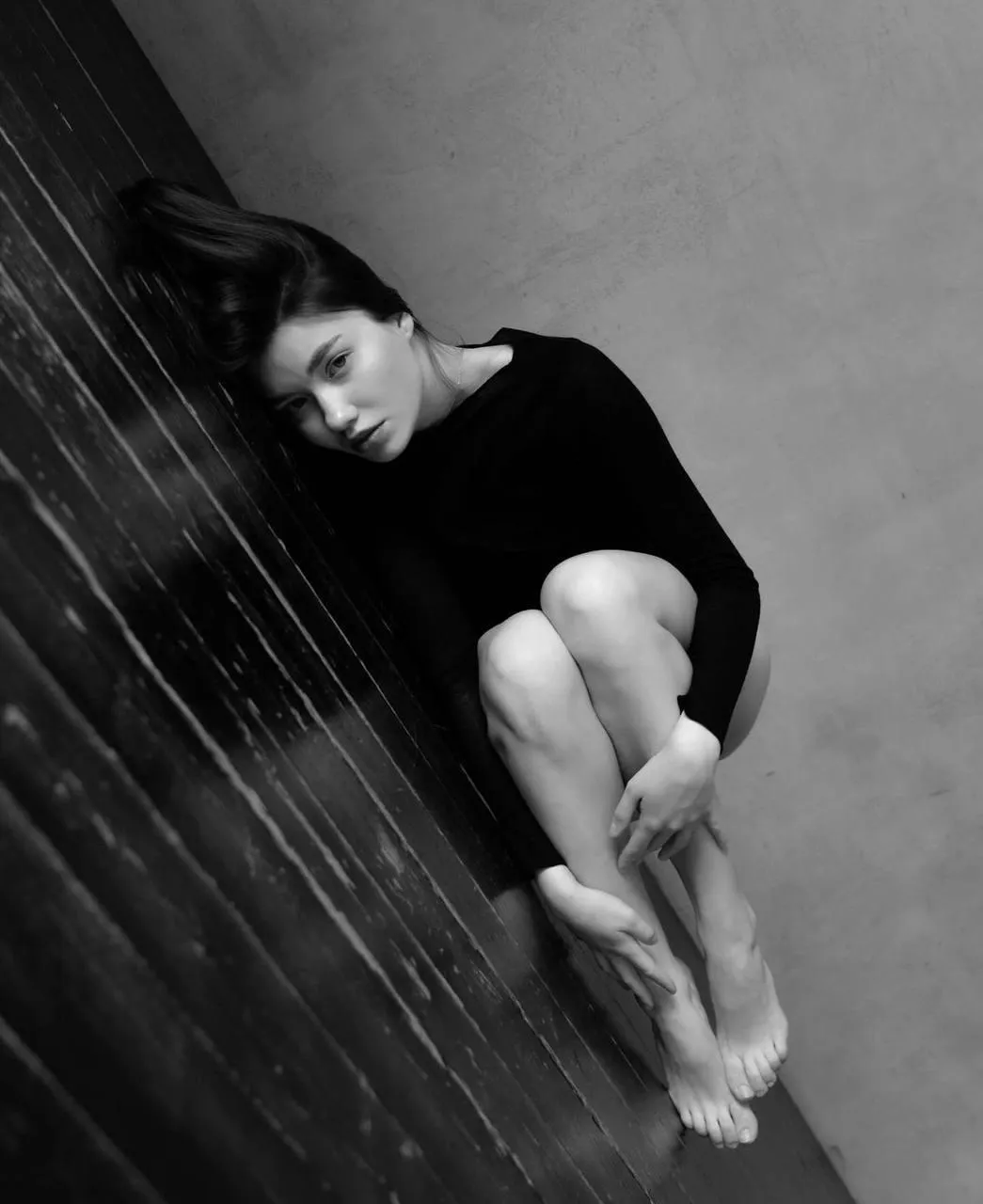 Black and white photo of a woman crouching on dark stairs