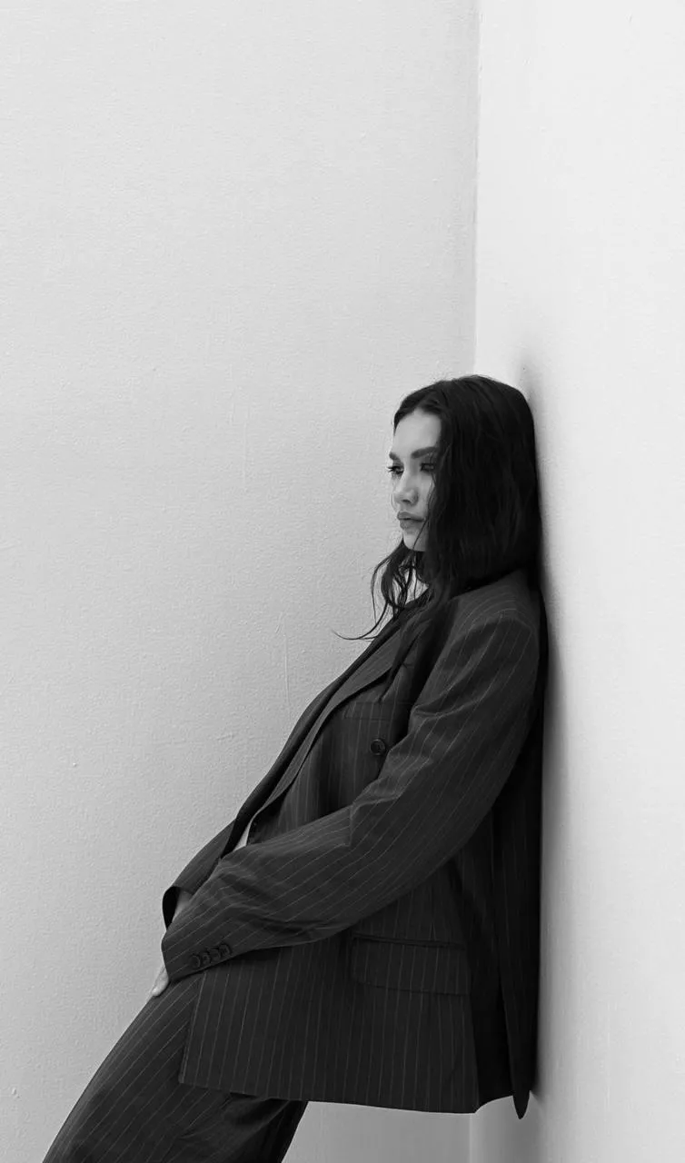 Black and white photo of a woman leaning against white wall