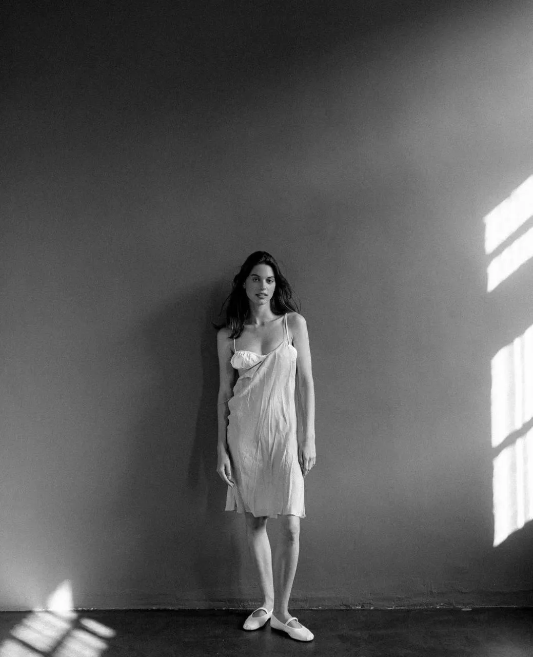 Black And White Photo of a Woman Standing Near a Sunlit Wall