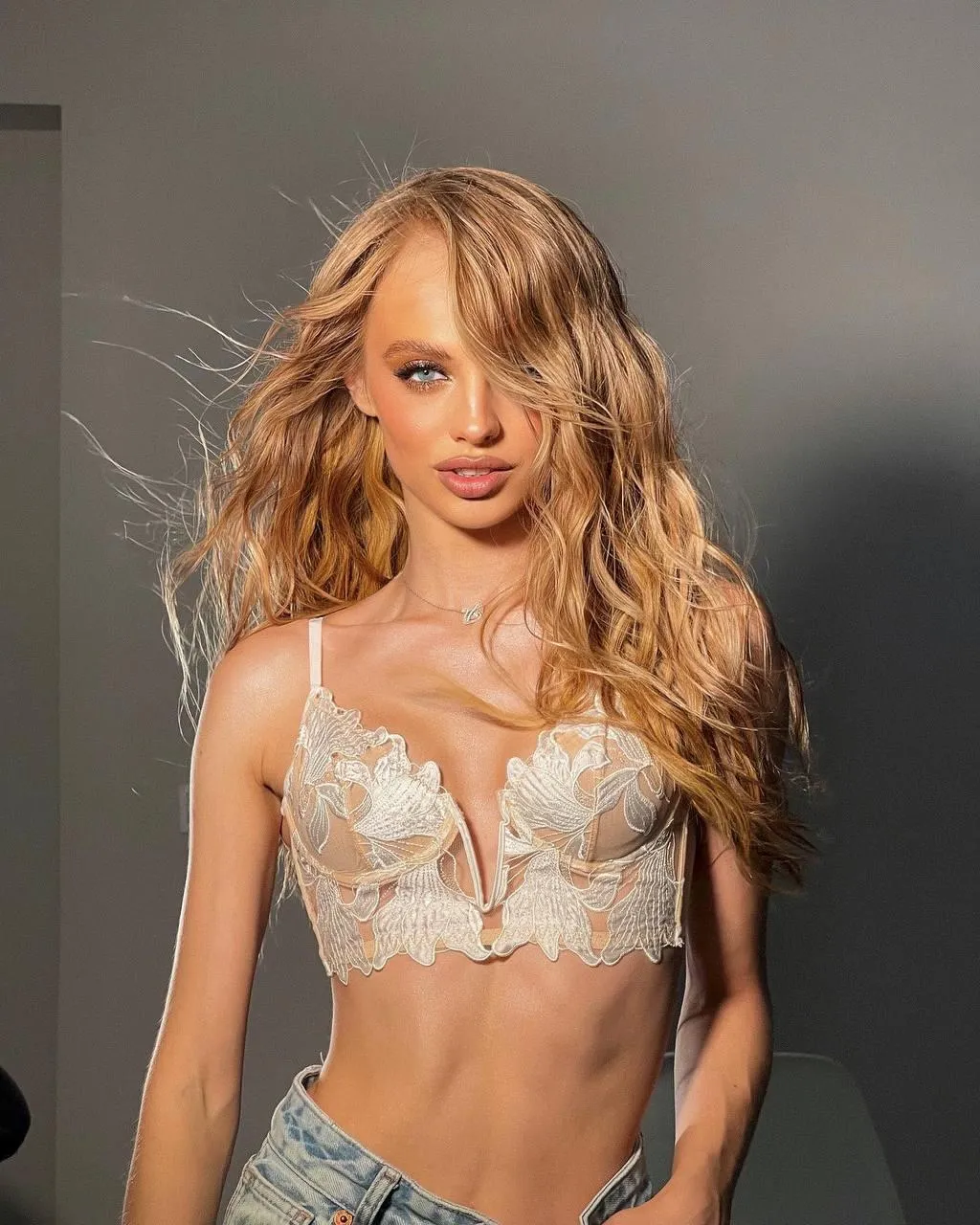 Blonde Model in a White Lace Top Posing Against Gray Wall