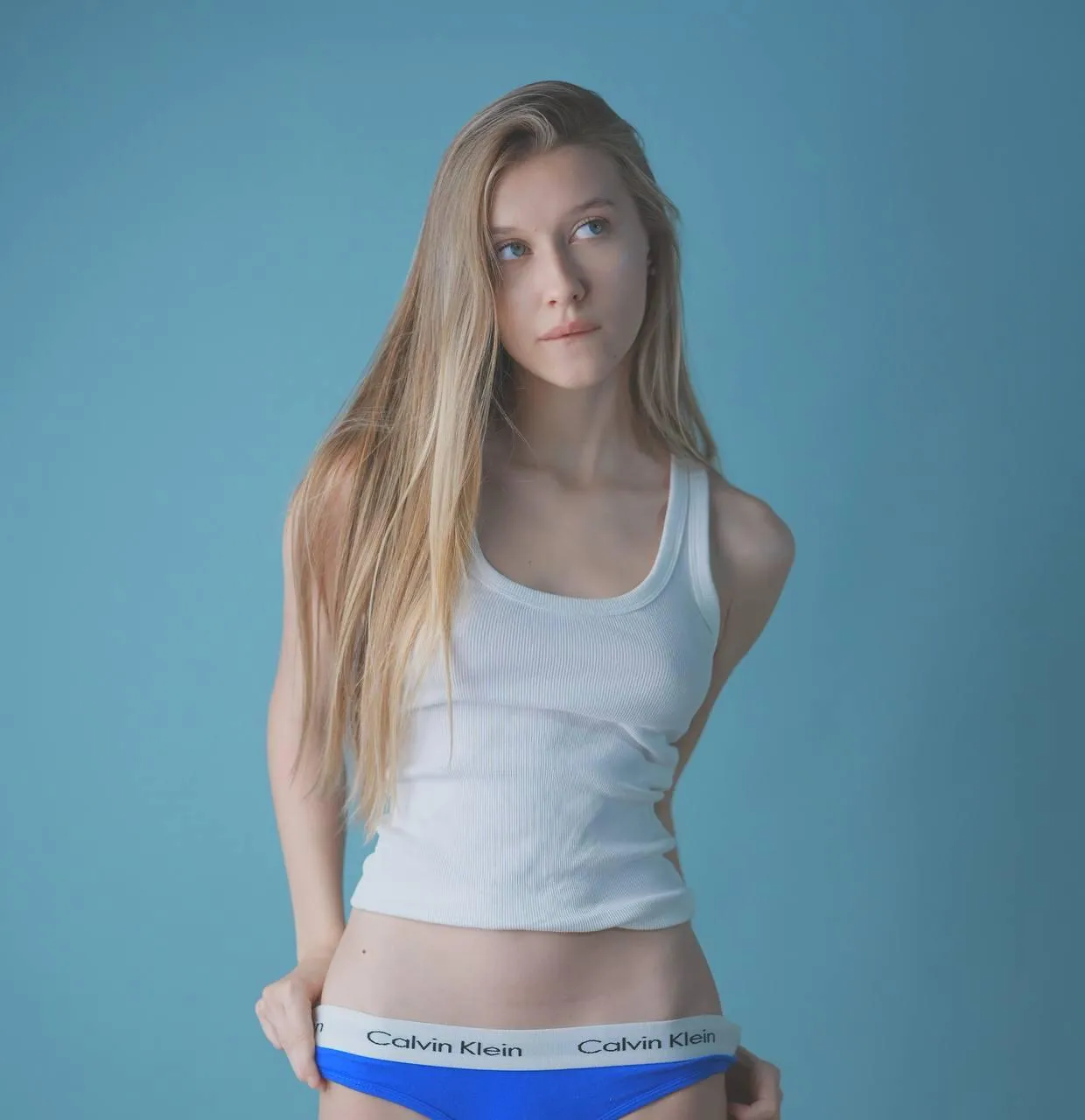 Blonde woman in a blue tank top with a soft blue background