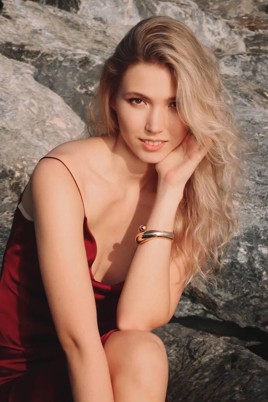 Blonde Woman in a Red Dress Posing by a Natural Stone Wall