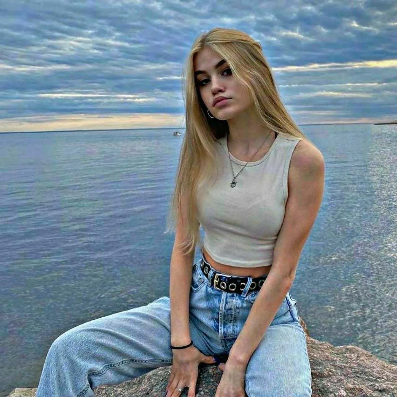 Blonde Woman Sits on a Rock Near a Calm Sea with a Breeze