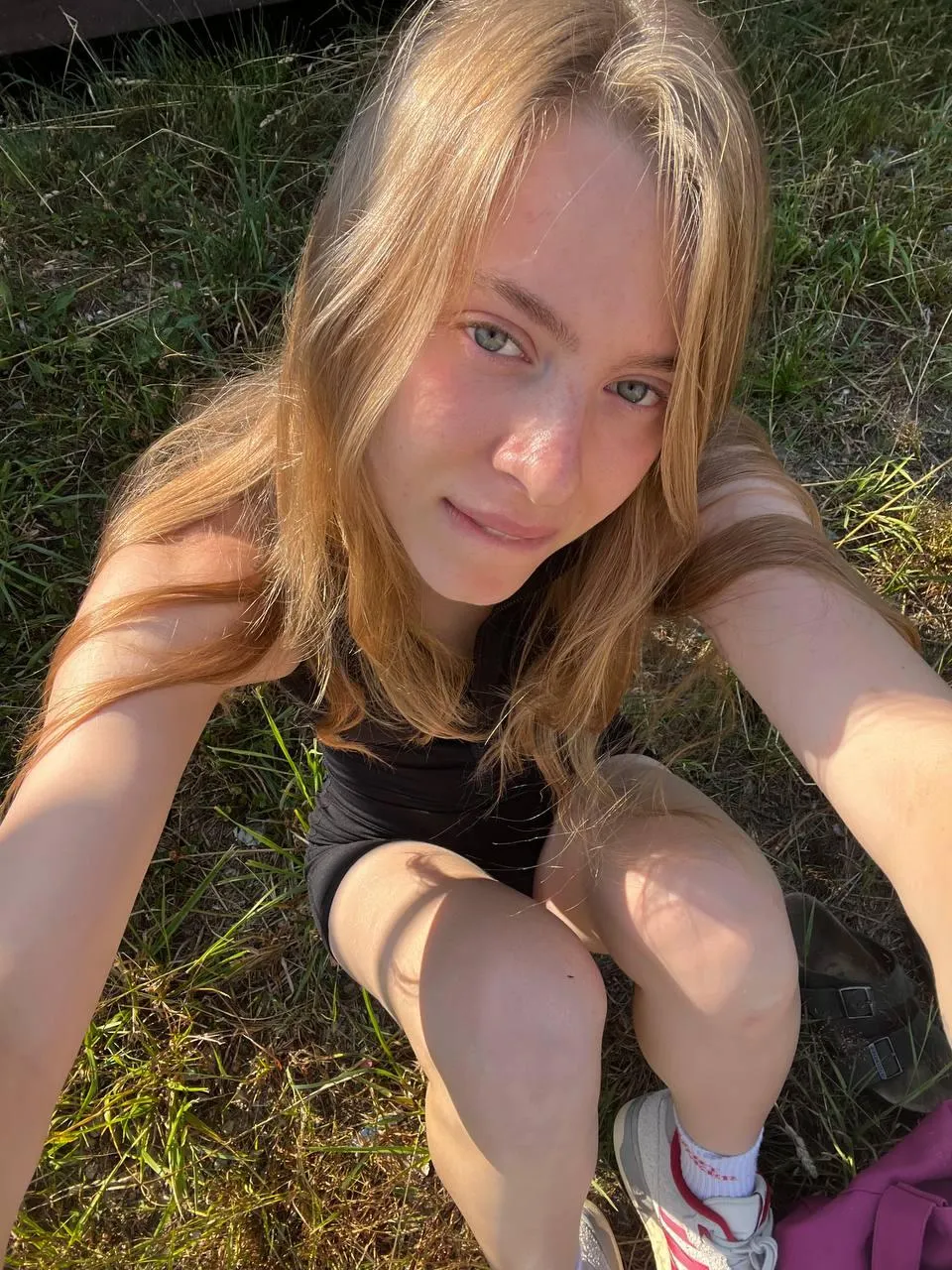 Blonde Woman Sitting on the Grass Looking Up at the Camera