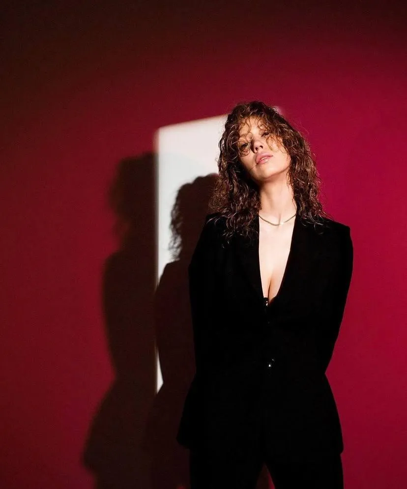 Bold woman in a black blazer near a red background wallpaper