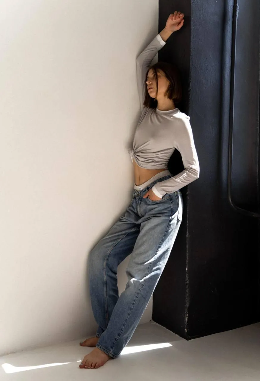Casual portrait of woman leaning against wall in loose jeans