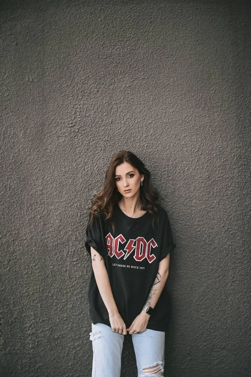 Casual Woman Stands by a Grey Wall Wearing a Black Tee Image