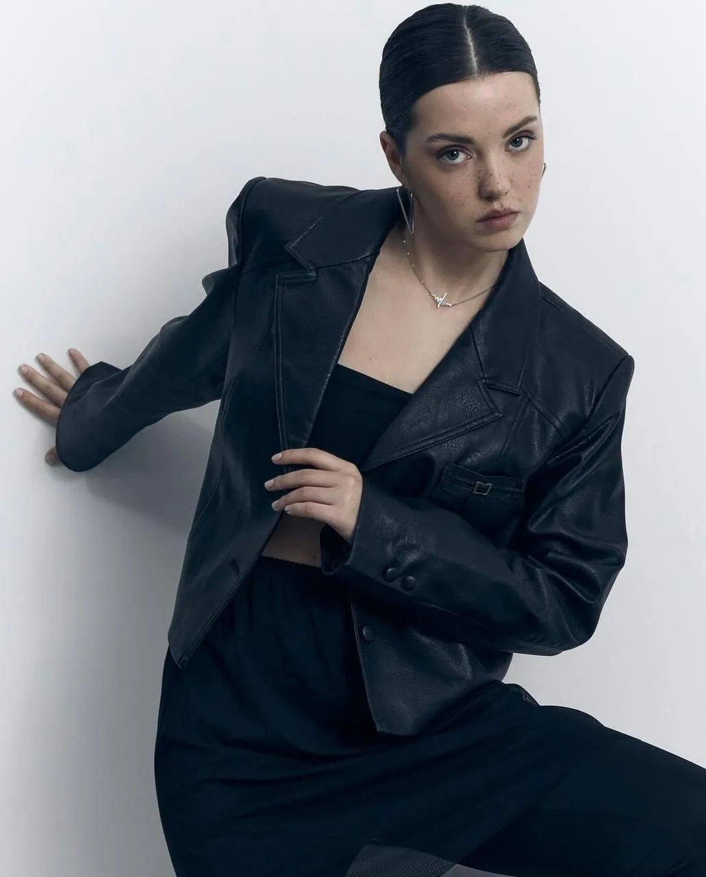 Confident woman in a black outfit leaning on the wall image