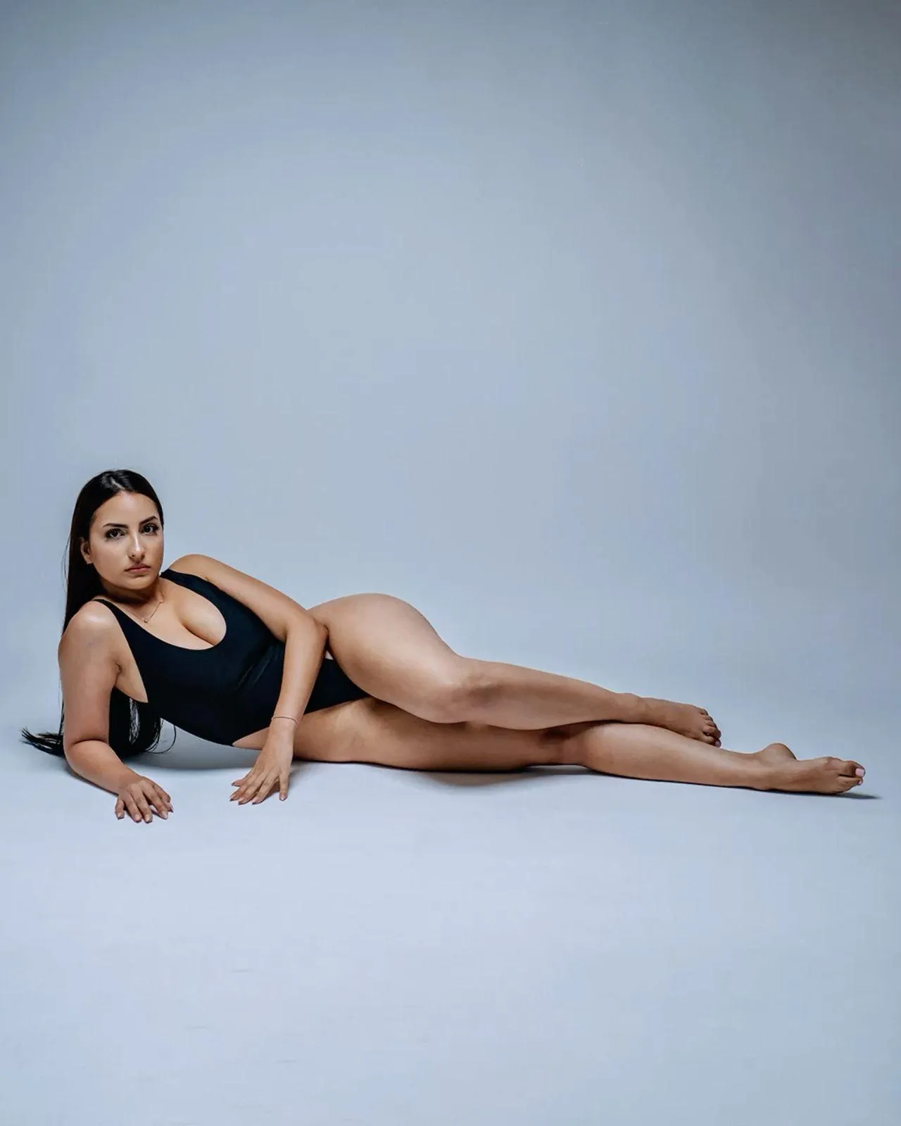 Confident woman posing on studio floor in a black swimsuit