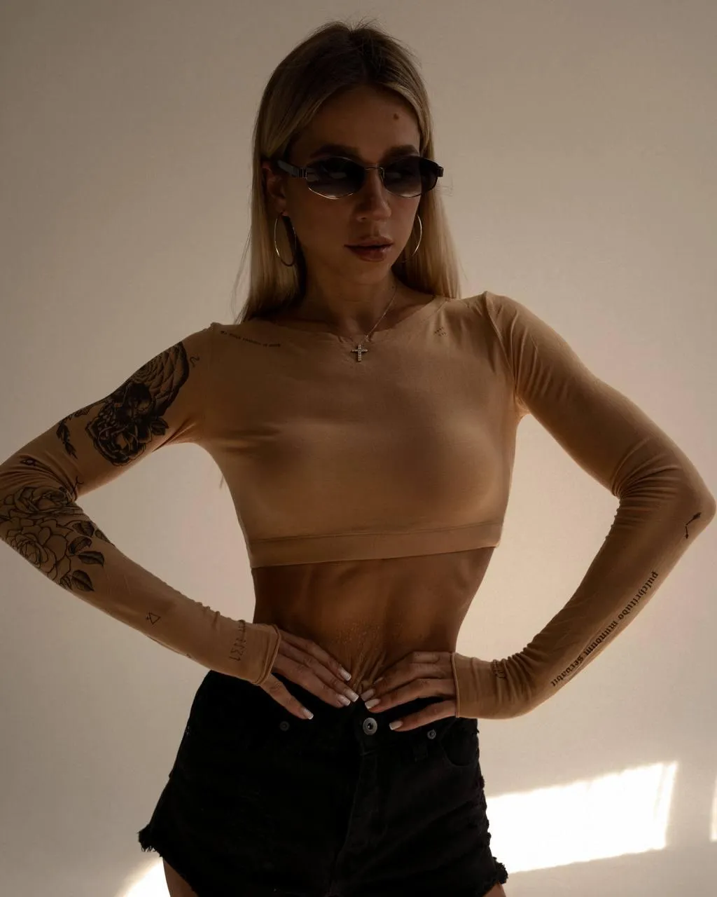 Confident woman with sunglasses posing near a white backdrop