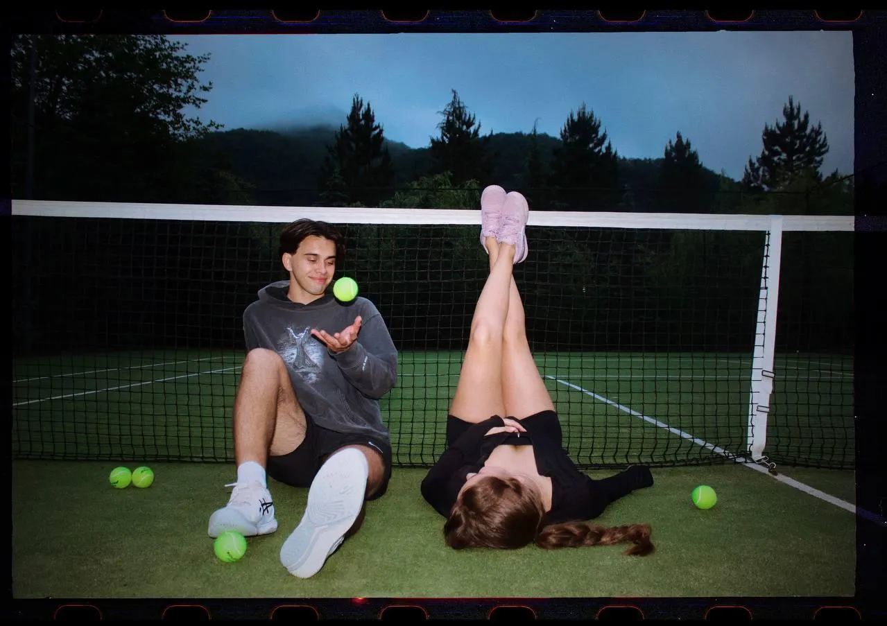 Couple Playing Tennis Sitting on the Court Legs Up Smiling