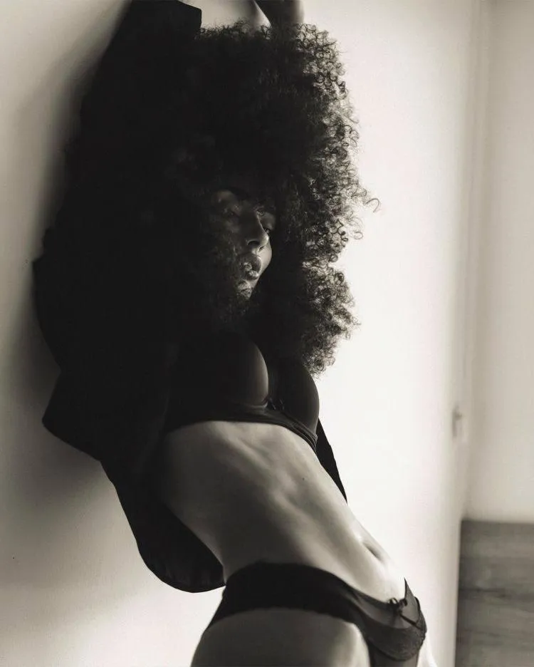 Curly hair woman stretching her body while lying on the wall