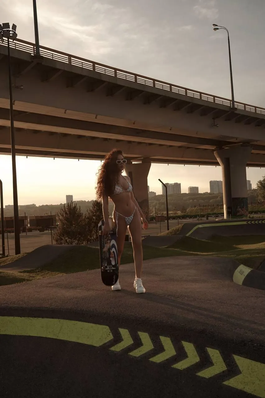 Curly Haired Woman in a Bikini Holding Skateboard at Sunset