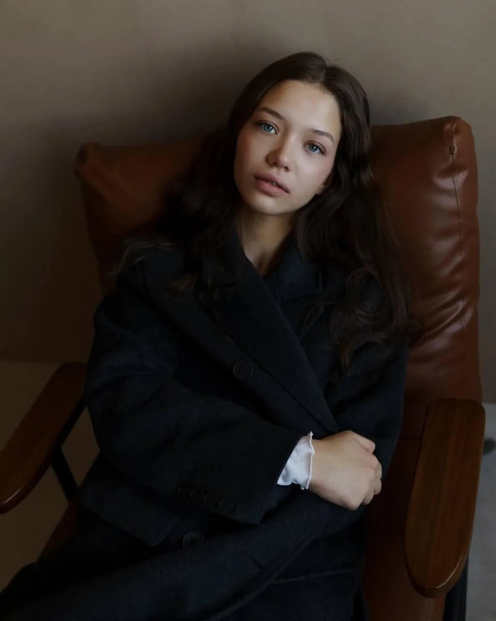 Cute girl wearing a black coat sitting on brown leather sofa