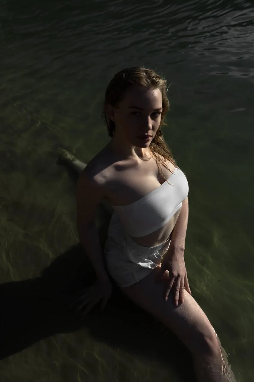 Cute woman in a white dress sitting on the calm water image