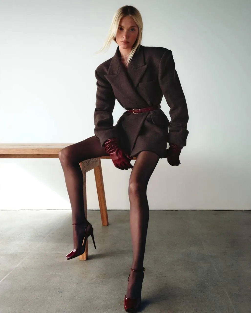 Elegant fashion model sitting on a desk in a formal outfit