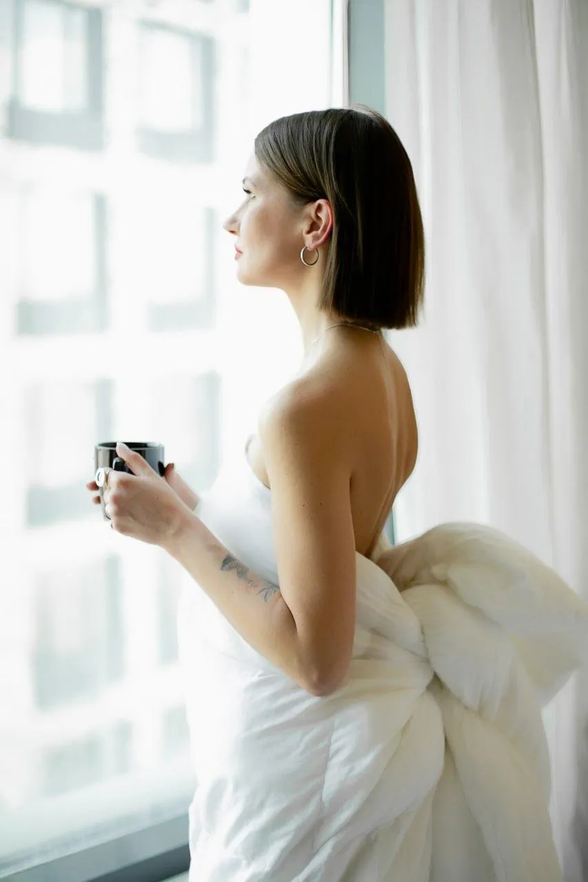 Elegant woman in a towel standing by the window with perfume