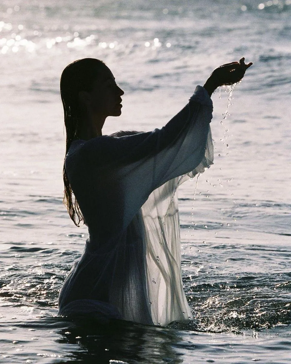Elegant Woman in a White Dress Standing Near the Ocean Waves