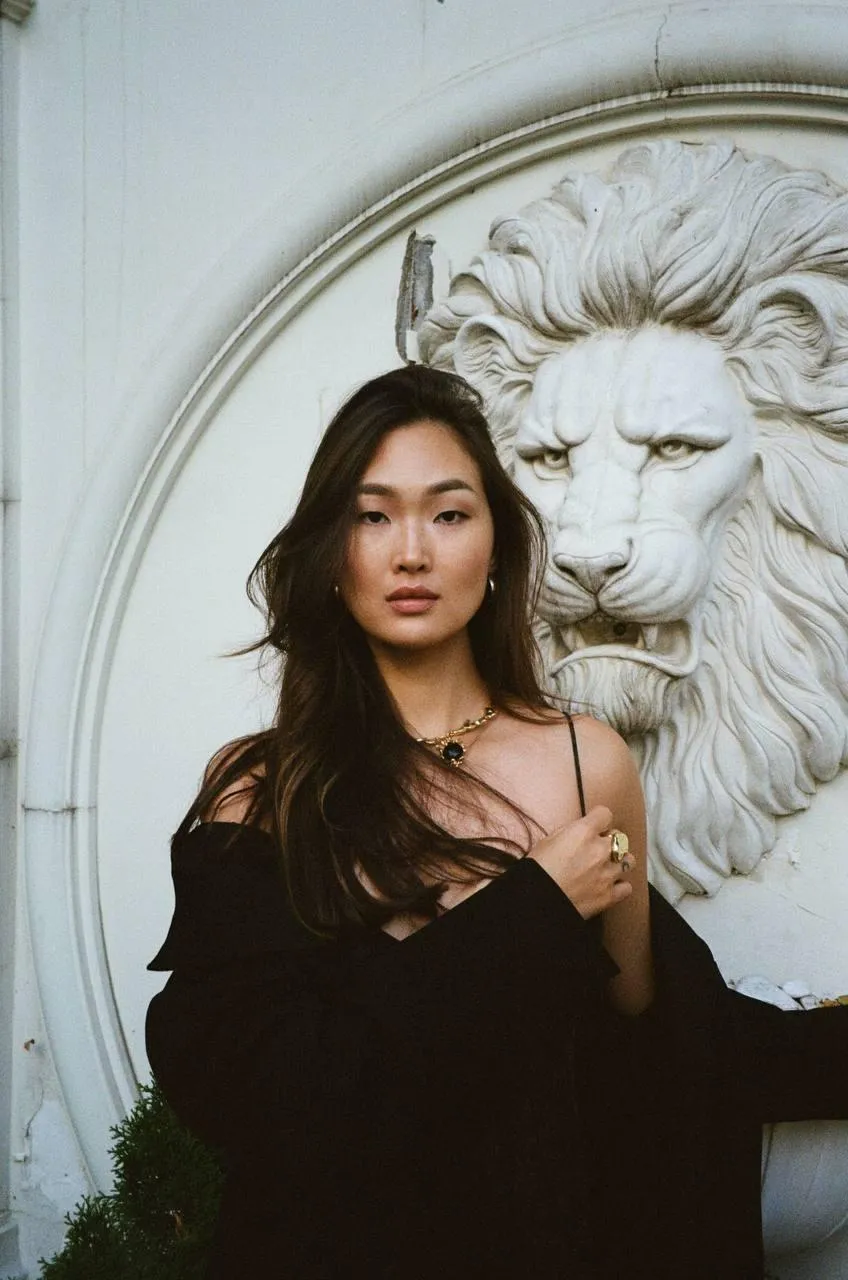 Elegant Woman Posing by a Lion Statue in a Dark Outfit Image