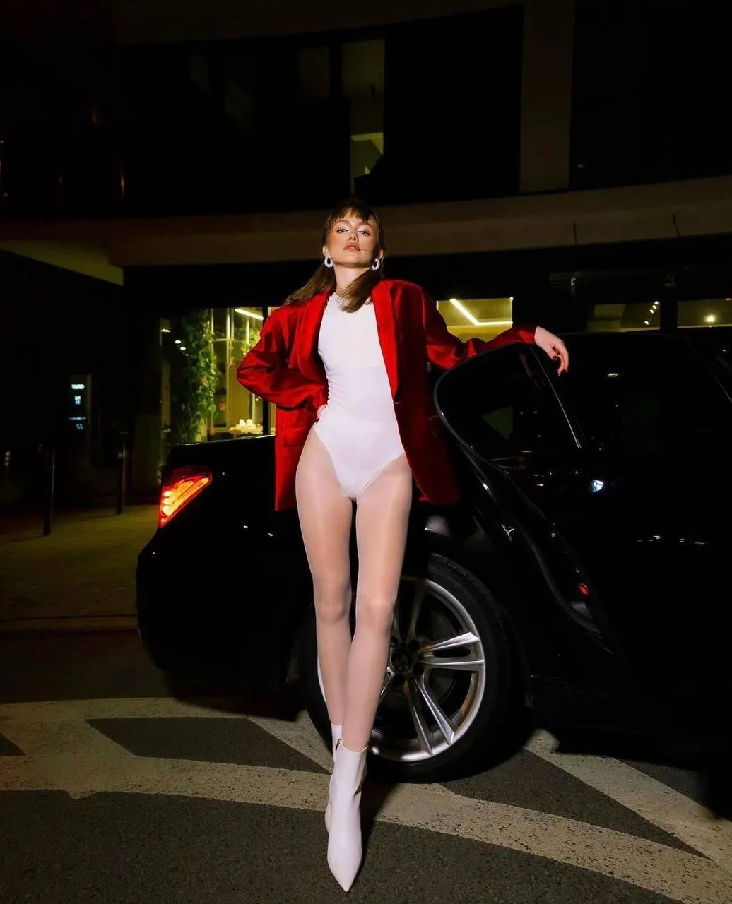 Fashion Model Posing in a Red Jacket Beside a Black Car