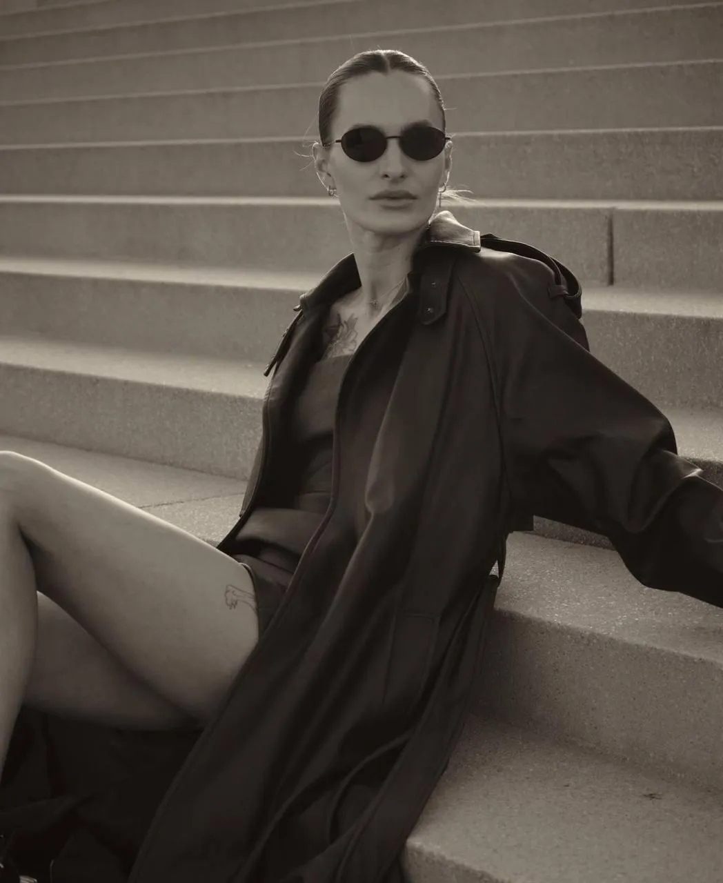 Fashionable woman in a trench coat sitting on outdoor stairs