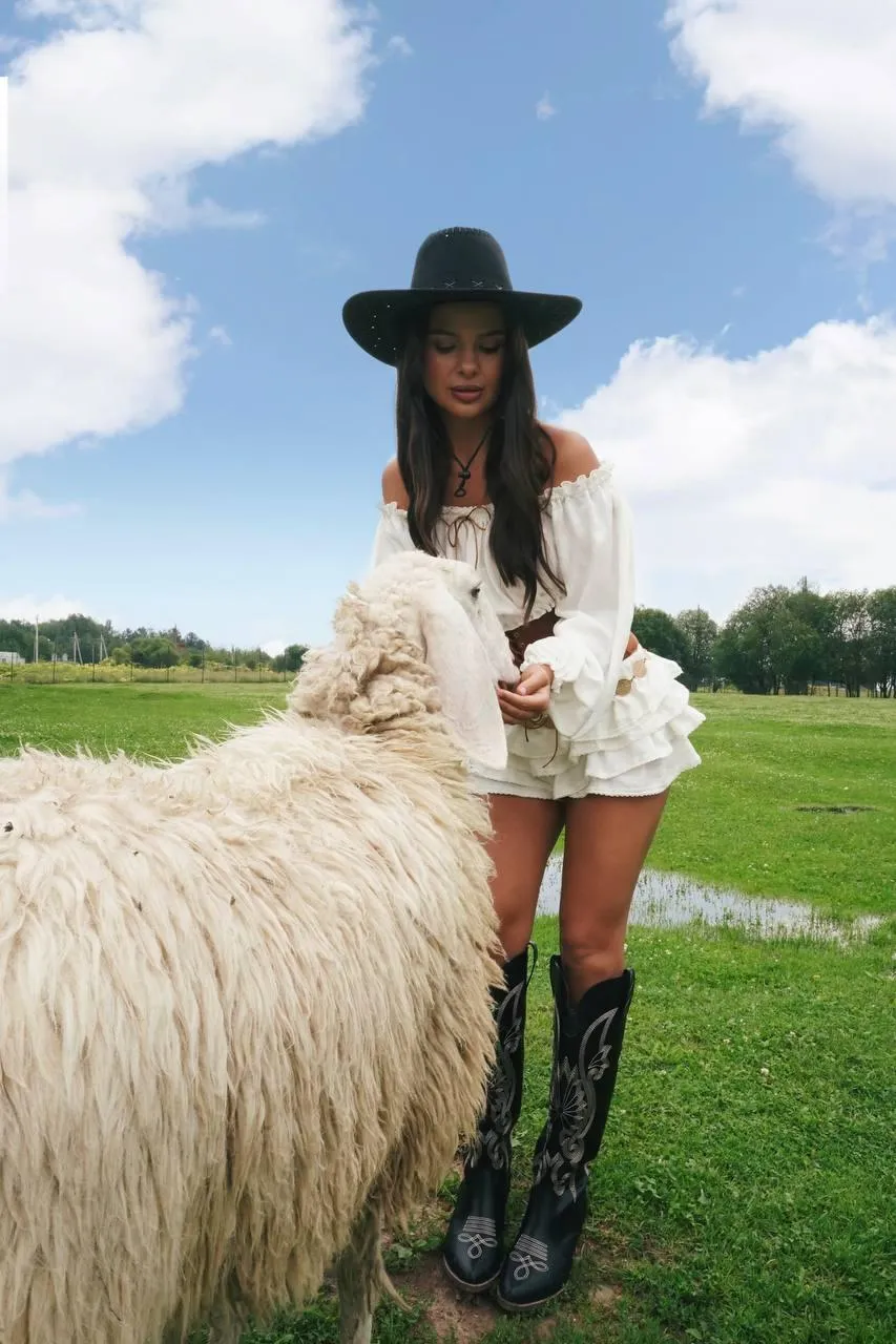 Fashionable Woman with a Hat Posing Near a Grazing Llama