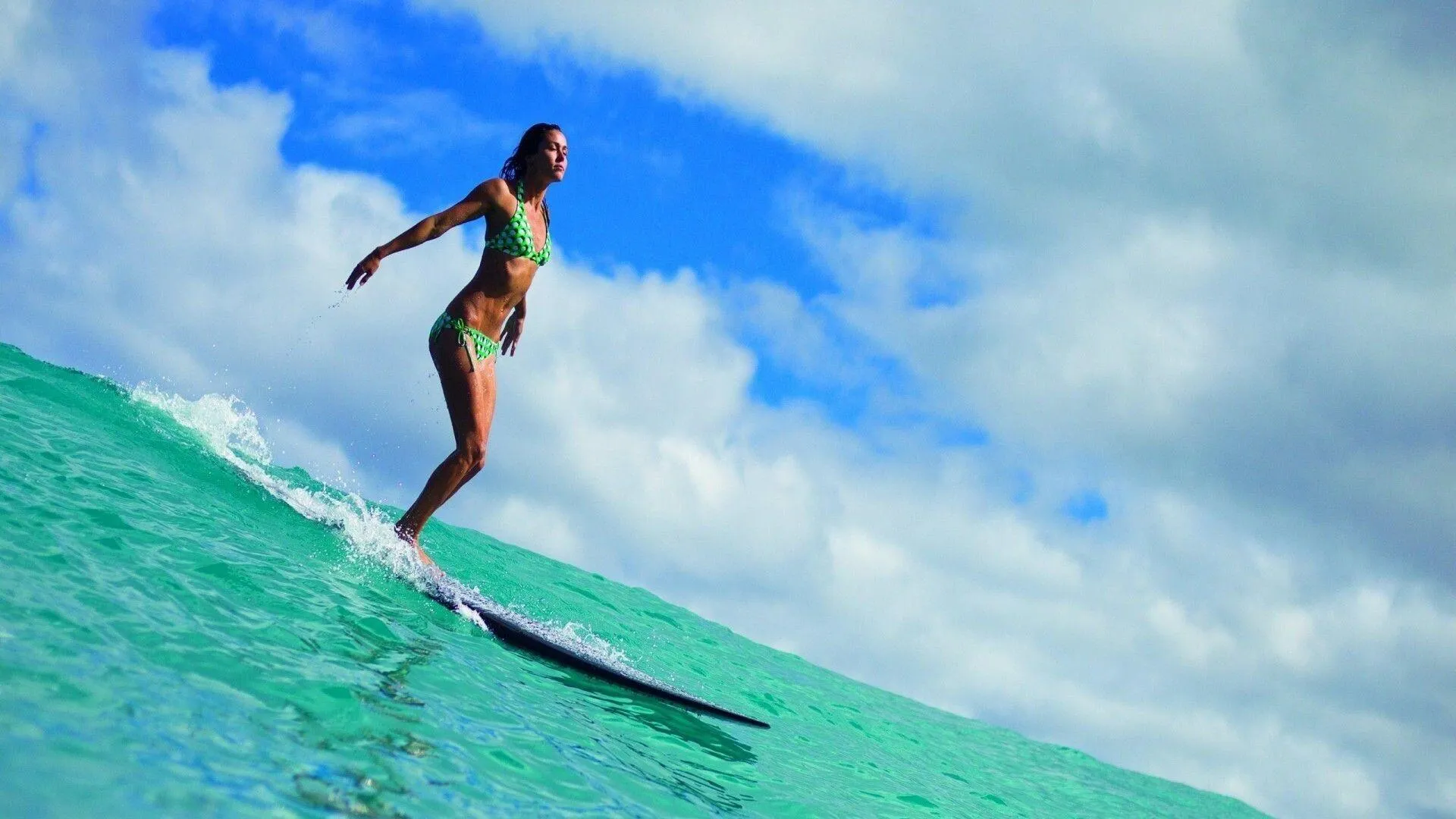 Female Surfer Gliding on a Wave Under a Blue Sky Wallpaper